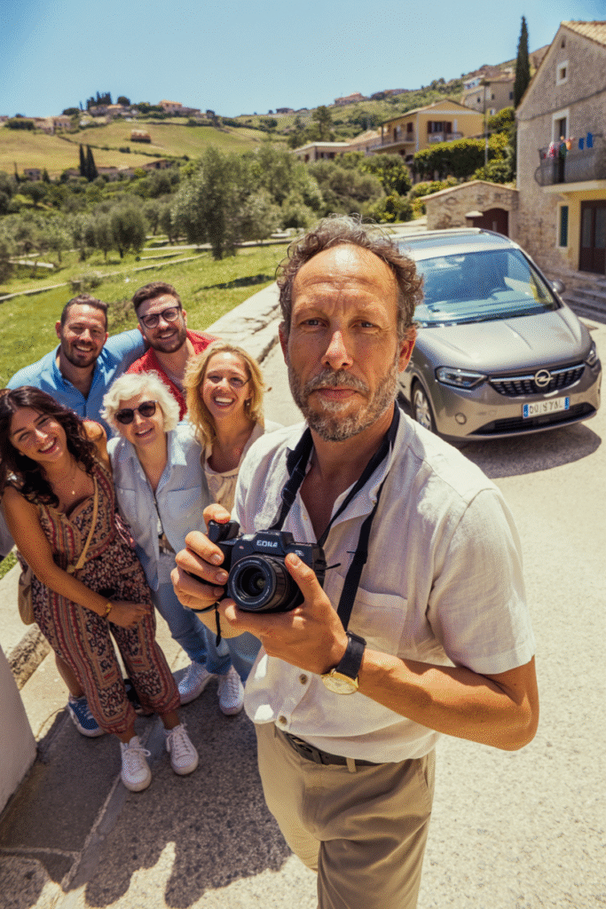 Guide sicilien souriant en selfie avec un groupe de voyageurs devant un paysage de Sicile et un minivan.